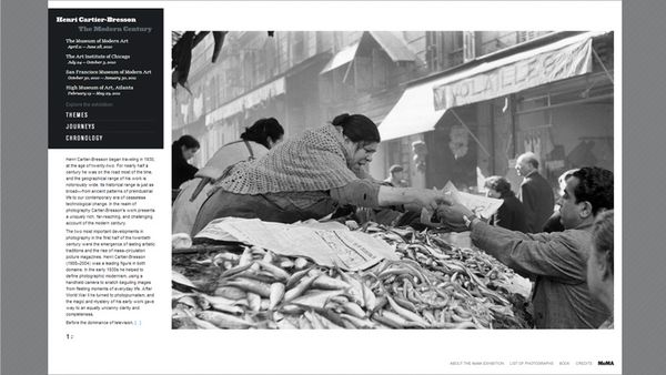 Screenshot of a website showing a large black and white photograph. Woman hands fish to a customer on a fish market.